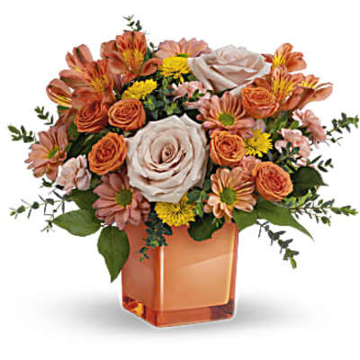Orange and blush bouquet in a square amber vase