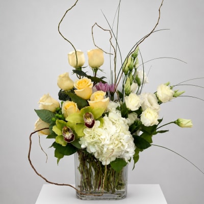 Mixed bouquet of yellow roses, white hydrangea, and orchids in a glass vase