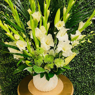 Tall white floral arrangement in a white vase with green accents