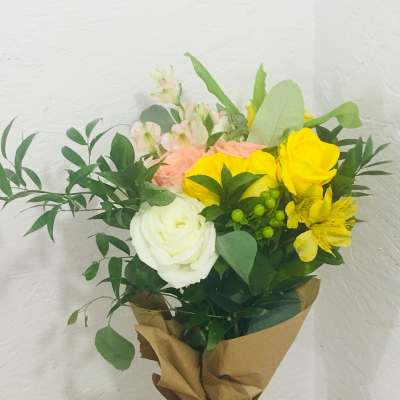 Bouquet of yellow and white roses with pink blooms in brown paper