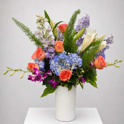 Colorful mixed bouquet in a white vase with roses, lilies, hydrangeas, and orchids