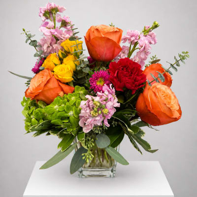 Mixed bouquet of orange and yellow roses with pink blooms in a glass vase