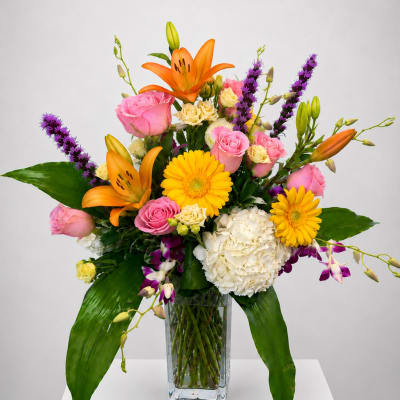 Mixed bouquet of orange lilies, pink roses, and yellow daisies in a glass vase