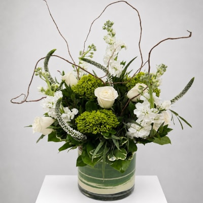 White roses and green blooms in a glass vase with curly branches