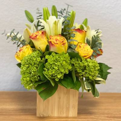 Yellow roses and white lilies in a wooden cube vase with green hydrangeas