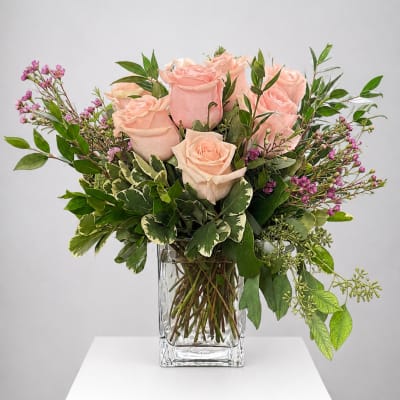 Blush pink roses in a clear glass vase with mixed greenery
