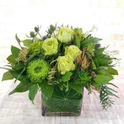 Green floral arrangement in a square glass vase with pale roses and chrysanthemums