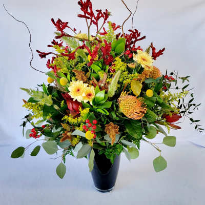 Large mixed floral arrangement in a black vase with red, yellow, and green blooms