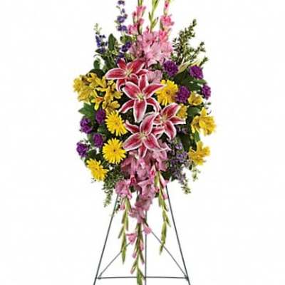 Standing floral spray with pink lilies, yellow daisies, and purple flowers on an easel