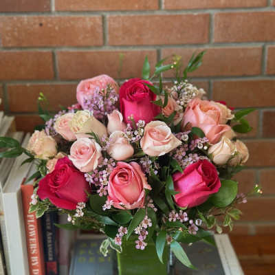 Rounded arrangement of pink and cream roses with tiny pink blossoms in a square glass vase