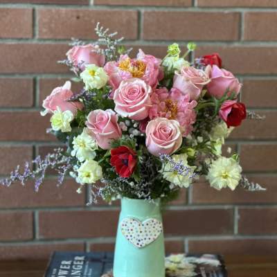 Pink roses and mixed flowers in a mint vase with a heart decoration