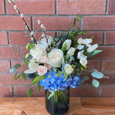 Vase arrangement of white roses, tulips, and blue hydrangeas with pussy willow branches