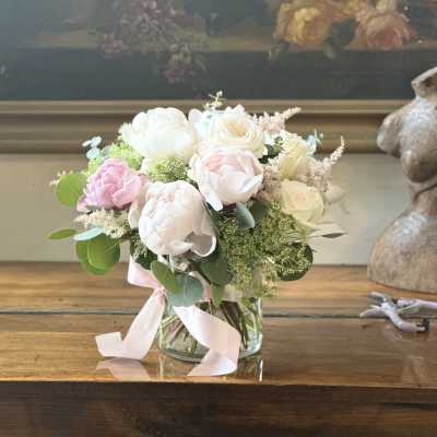 Pastel bouquet of peonies and roses in a glass vase with a pink ribbon