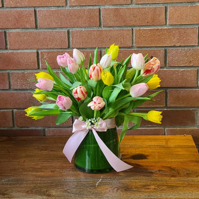 Bouquet of pink and yellow tulips in a glass vase with a pink ribbon
