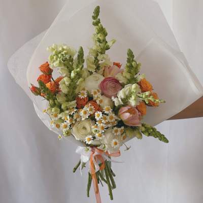 Hand-tied bouquet of orange, white, and pink flowers wrapped in white paper