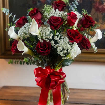 Bouquet of red roses and white calla lilies in a glass vase with a red ribbon