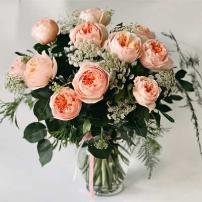 Peach garden roses and white filler flowers arranged in a clear glass vase