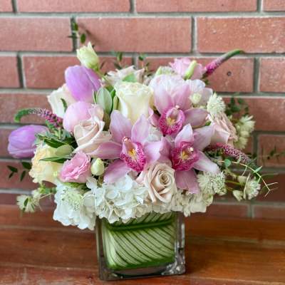 Pink and white bouquet with orchids and roses in a square glass vase