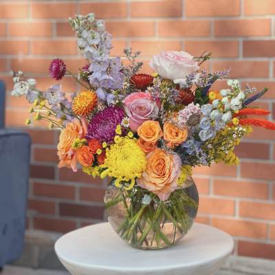 Mixed bouquet of roses, chrysanthemums, and delphinium in a glass vase