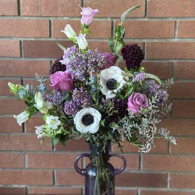 Mixed purple and white flowers arranged in a purple glass vase