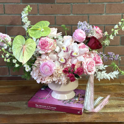 Pink and white floral arrangement in a white vase with ribbon