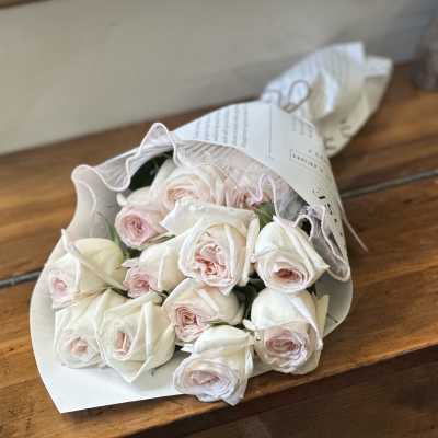 Bouquet of pale pink and white roses wrapped in white paper, resting on a wooden table
