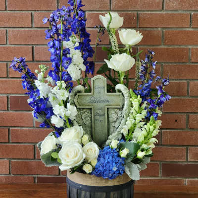 White roses and blue flowers arranged around a memorial cross in a basket