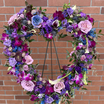 Heart-shaped floral wreath with purple, pink, and blue flowers on a stand
