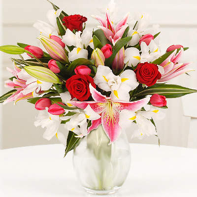 Bouquet of pink and white lilies with red roses in a clear glass vase