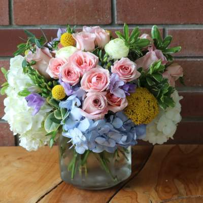 Bouquet of pink roses, hydrangeas, and yellow accents in a glass vase