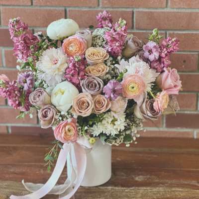 Pastel arrangement of roses, ranunculus, and peonies in a white vase with ribbon