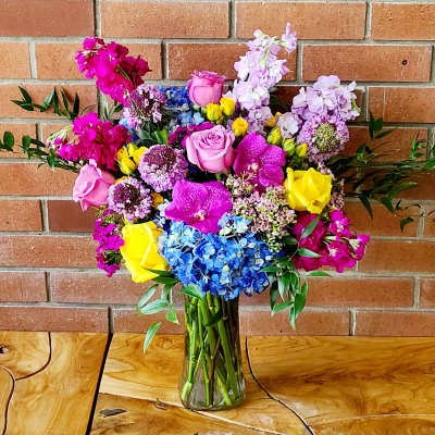 Colorful bouquet of roses, orchids, hydrangeas, and purple blooms in a glass vase