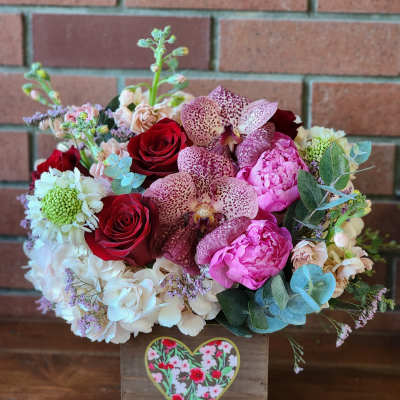 Mixed bouquet of red roses, pink blooms, and spotted orchids in a wooden box