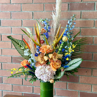 Tropical bouquet in a tall green vase with orange and blue flowers