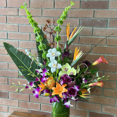 Tropical flower arrangement in a green glass vase with orchids and lilies