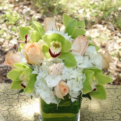 Bouquet of pale roses, white hydrangeas, and green orchids in a square glass vase