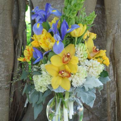 Bouquet of yellow orchids, blue irises, and white blooms in a glass vase
