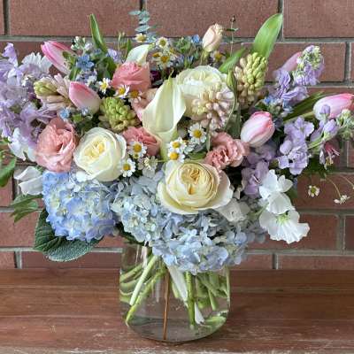 Pastel bouquet of roses, tulips, hydrangeas, and lilies in a glass vase