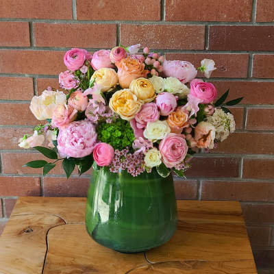 Mixed pastel flower arrangement in a green glass vase