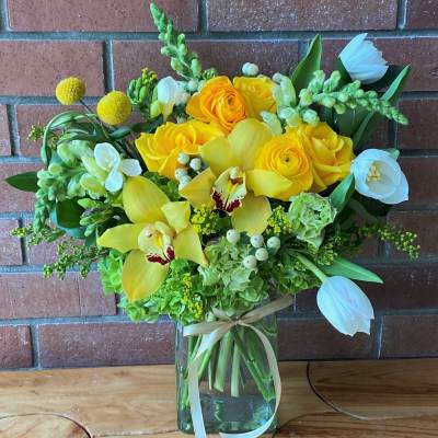 Yellow and white floral arrangement in a glass vase with a ribbon