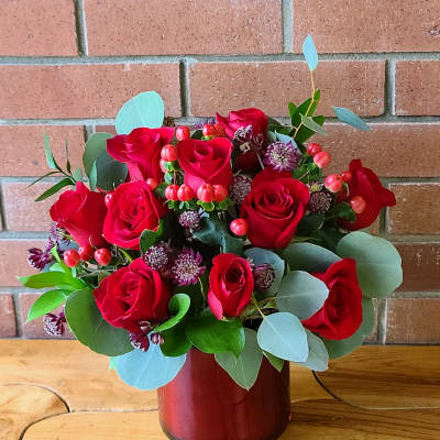 Red roses arranged in a red vase with eucalyptus and small accent flowers