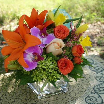 Bright mixed bouquet with orange lilies, roses, and purple orchids in a glass vase