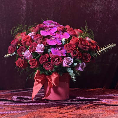 Pink and red rose arrangement with orchids in a round box tied with a ribbon