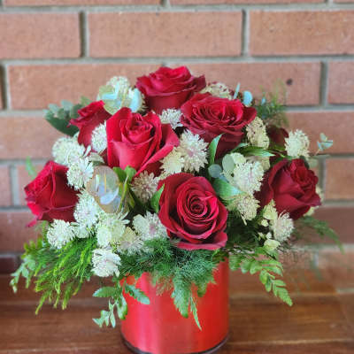 Red roses arranged in a red vase with white filler flowers