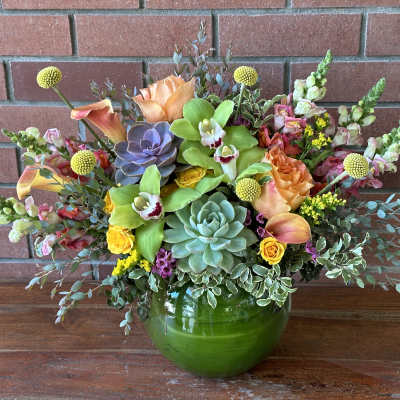 Mixed floral arrangement in a green glass vase with succulents and orchids