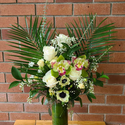 Tall floral arrangement with white roses and orchids in a green vase
