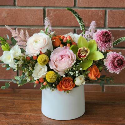 Mixed floral arrangement in a white vase with pink, white, orange, and green blooms