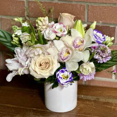 Mixed bouquet of cream, white, and purple flowers in a white vase