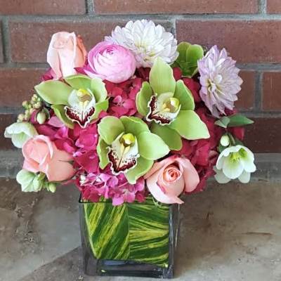 Pink and green floral arrangement in a square glass vase