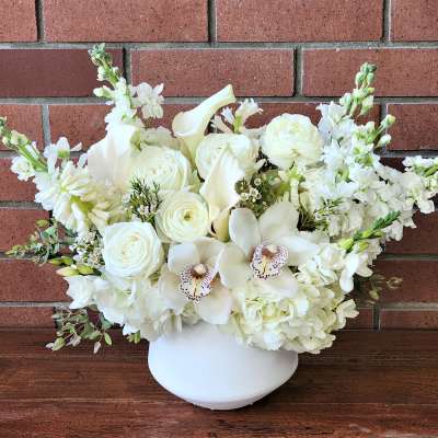 White floral arrangement in a white vase with roses and orchids